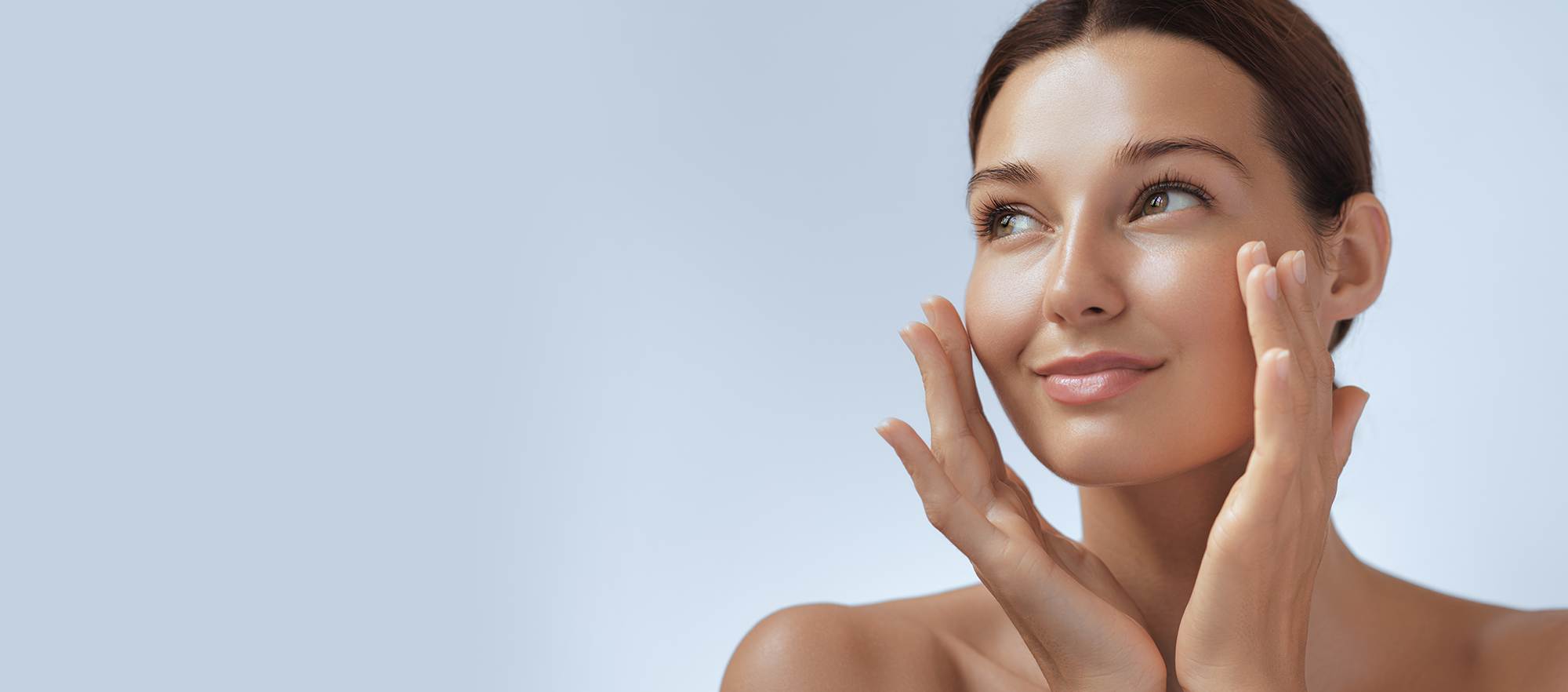 Image of woman with brown hair and glowy skin touching her face